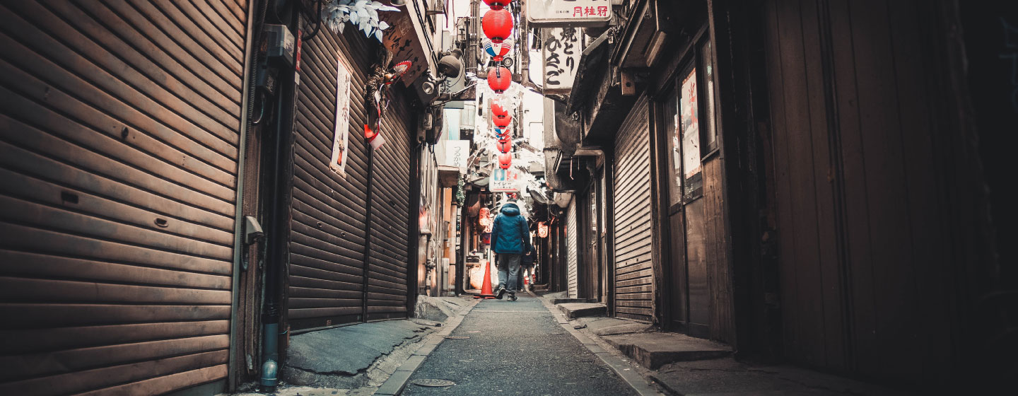 Individual walks through an alley with Chinese lanterns hanging above