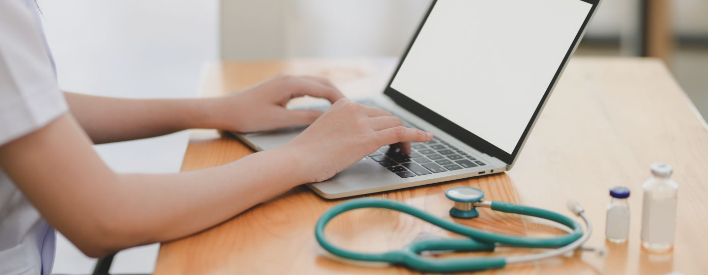 Laptop near teal stethoscope in wooden table.