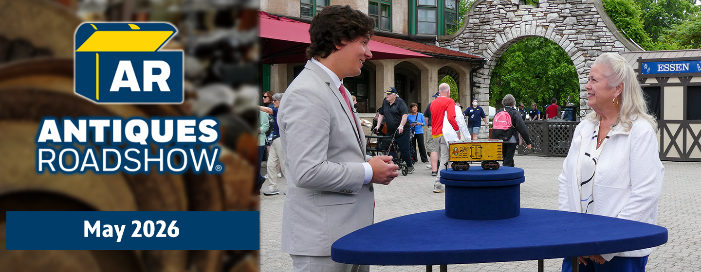 A man and woman discussing a toy train car, also includes the Antiques Roadshow logo with the text May 2026.